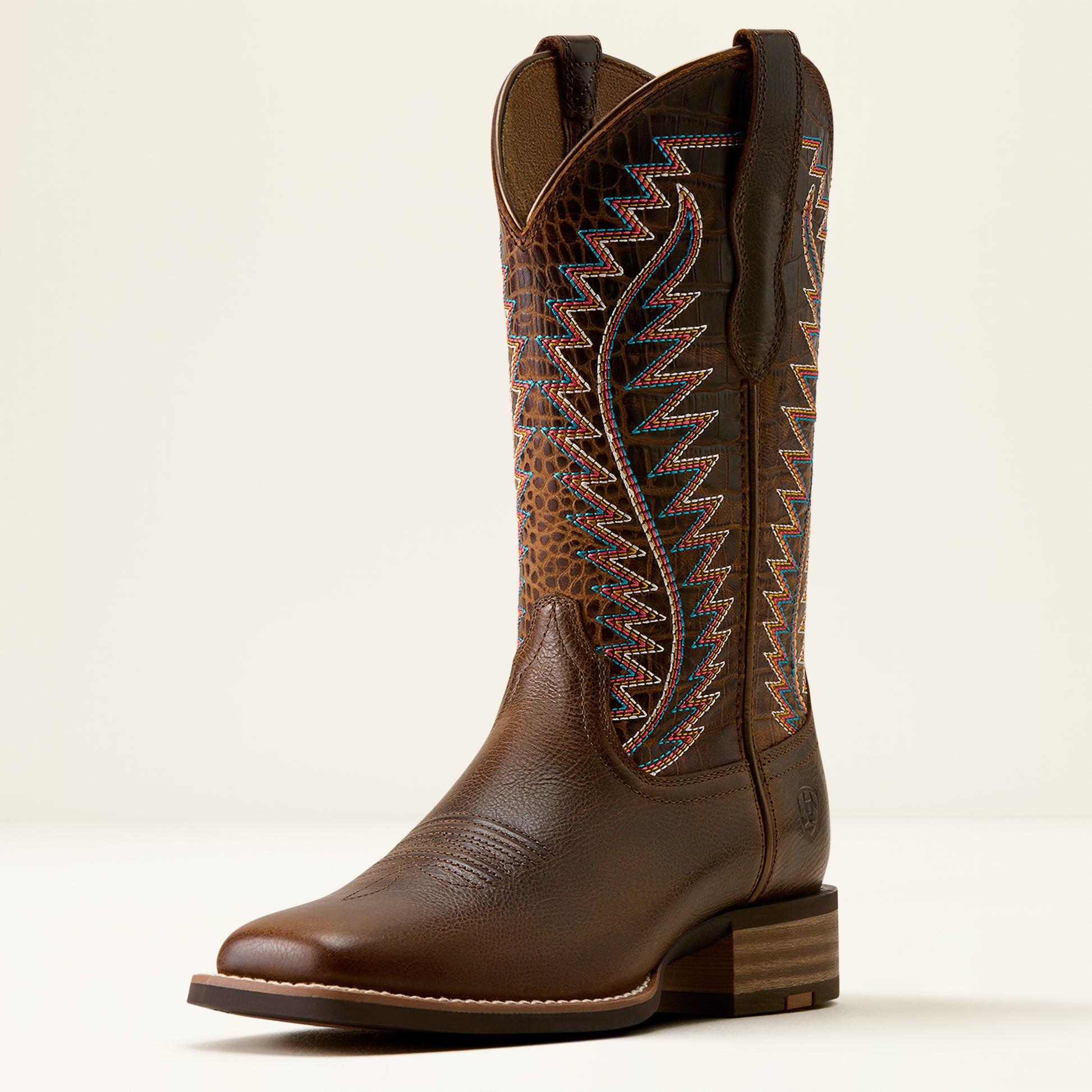 A single brown leather cowboy boot with decorative embroidered shaft detailing, shown in a side profile against a clean, light beige background.