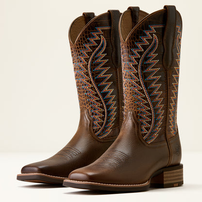 A pair of brown leather cowboy boots with decorative embroidered shafts in blue, orange, and gold, shown on a light beige background.