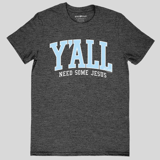 A dark heather gray t-shirt from Grace & Truth with a graphic on the chest that reads 'Y'ALL NEED SOME JESUS' in light blue and white text, shown against a solid light gray background.