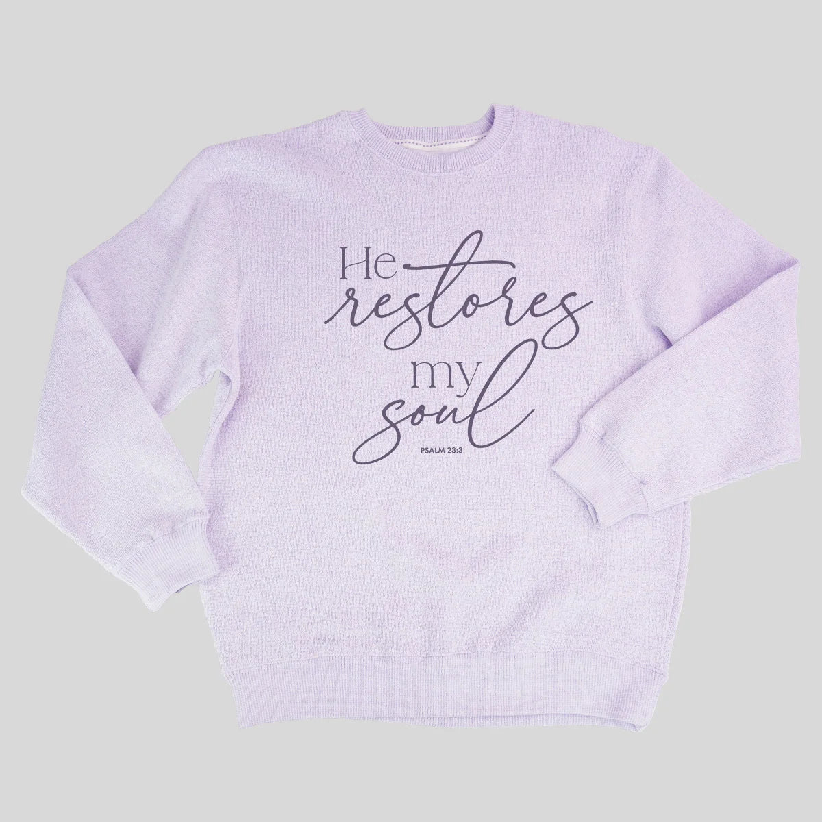 A light lavender crewneck sweatshirt from Grace & Truth featuring the printed text 'He restores my soul' in black script and serif fonts, with 'PSALM 23:3' printed below in a small block font, displayed on a solid light gray background.