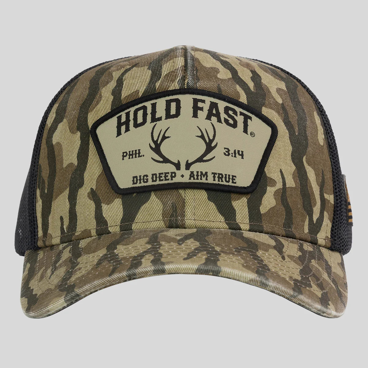 A camouflage trucker hat from Hold Fast with a black mesh back and a front patch that reads 'HOLD FAST' with antlers and 'DIG DEEP • AIM TRUE'.