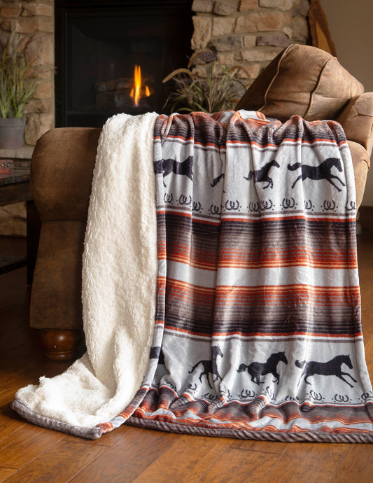 A fleece throw blanket with a horse pattern, draped over a chair and a sofa, in a cozy living room setting, with a fireplace and plants in the background.