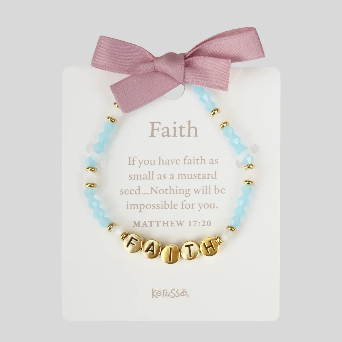 A beaded bracelet with light blue and white beads, gold spacer beads, and gold letter beads spelling 'FAITH', displayed on a white card with a pink ribbon bow. The card features the word 'Faith' and a Bible verse, with the brand name Kerusso