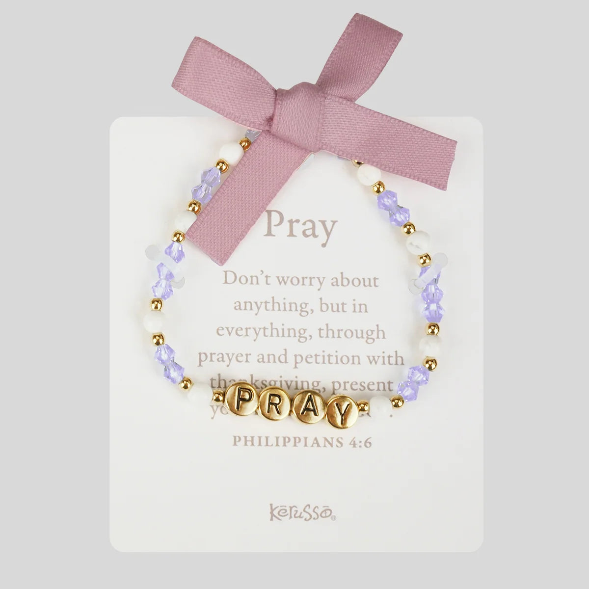 A beaded prayer bracelet with lavender beads, white pearls, and gold-toned letter beads spelling 'PRAY', displayed on a white card with a pink ribbon bow. The card features the word 'Pray' and a Bible verse, with the brand 'Kerusso' at the bottom.
