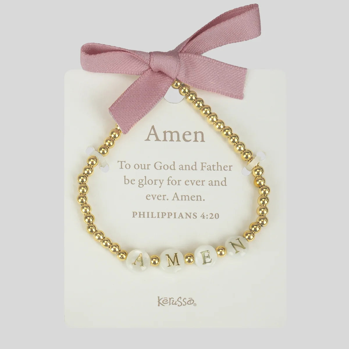 A gold beaded charm bracelet with white pearl-like beads spelling 'AMEN' and small letter beads, displayed on a cream card with a dusty pink ribbon bow. The card features the word 'Amen' and a Bible verse, with the brand name 'Kerusso' at the bottom.