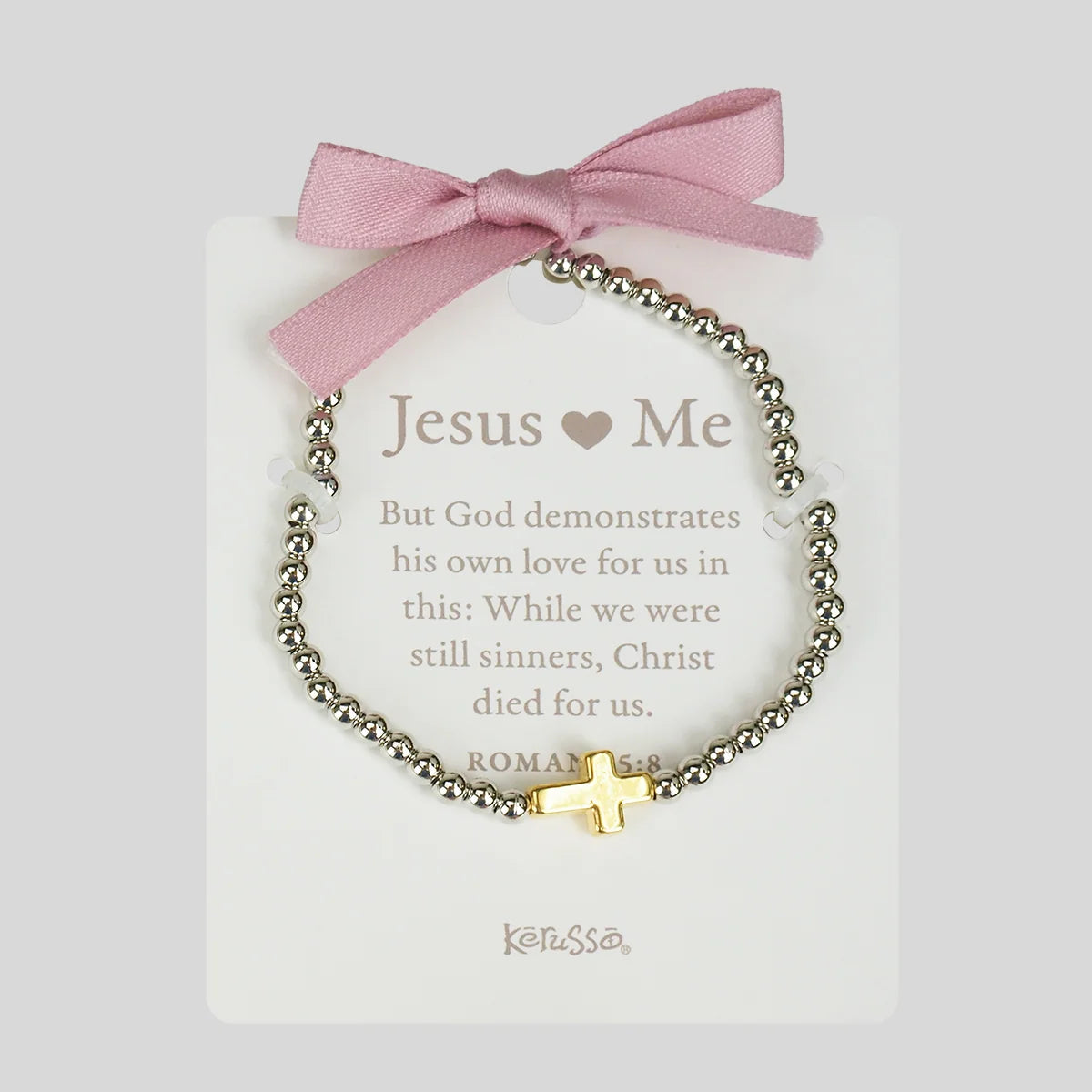 A beaded bracelet with a gold cross charm and white heart beads, displayed on a white card with a pink ribbon bow. The card reads 'Jesus ♥ Me' and shows the brand Kerusso