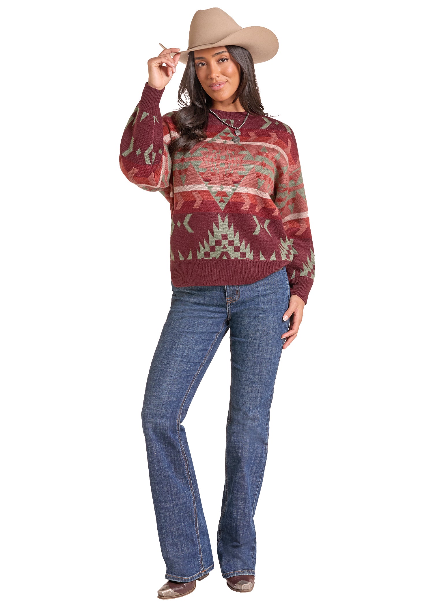  woman wearing a maroon knit sweater by Panhandle Slim with a Southwestern geometric pattern in sage green and beige, paired with a tan cowboy hat and blue jeans, against a plain white background.