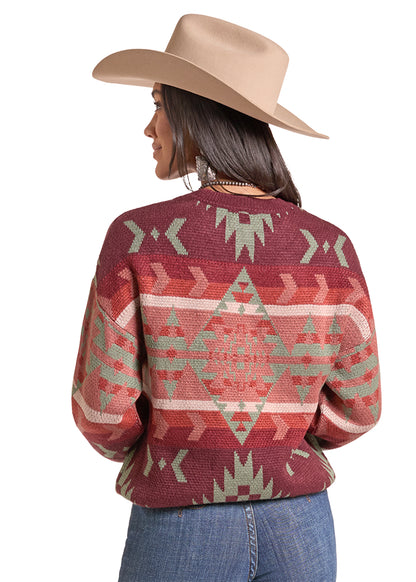  woman wearing a maroon knit sweater by Panhandle Slim with a Southwestern geometric pattern in sage green and beige, paired with a tan cowboy hat and blue jeans, against a plain white background.