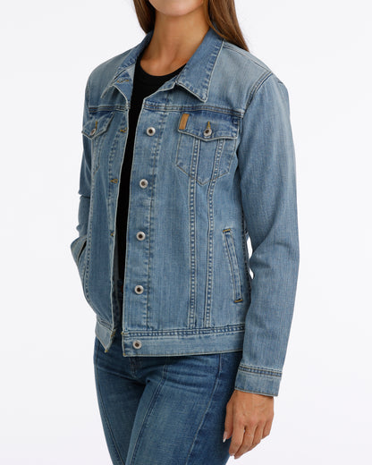 woman wearing a Cinch jean jacket, and blue jeans on a grey background
