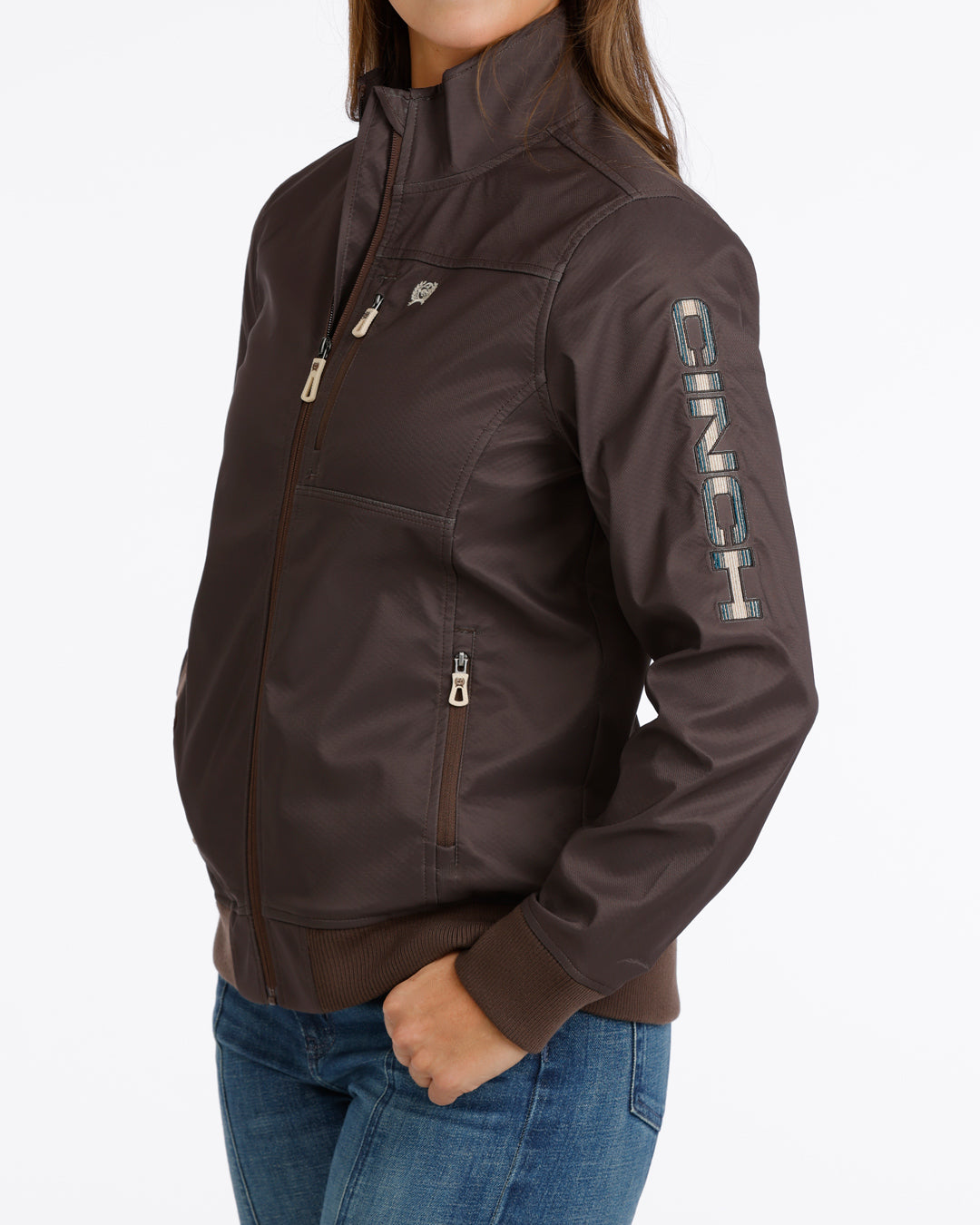 Woman wearing a brown Cinch jacket and blue jeans on a white background