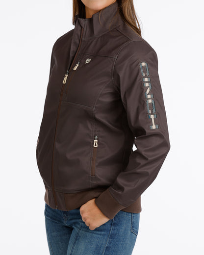 Woman wearing a brown Cinch jacket and blue jeans on a white background
