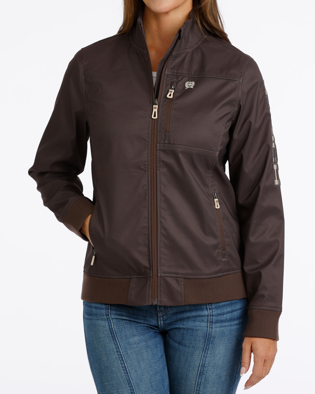 Woman wearing a brown Cinch jacket and blue jeans on a white background
