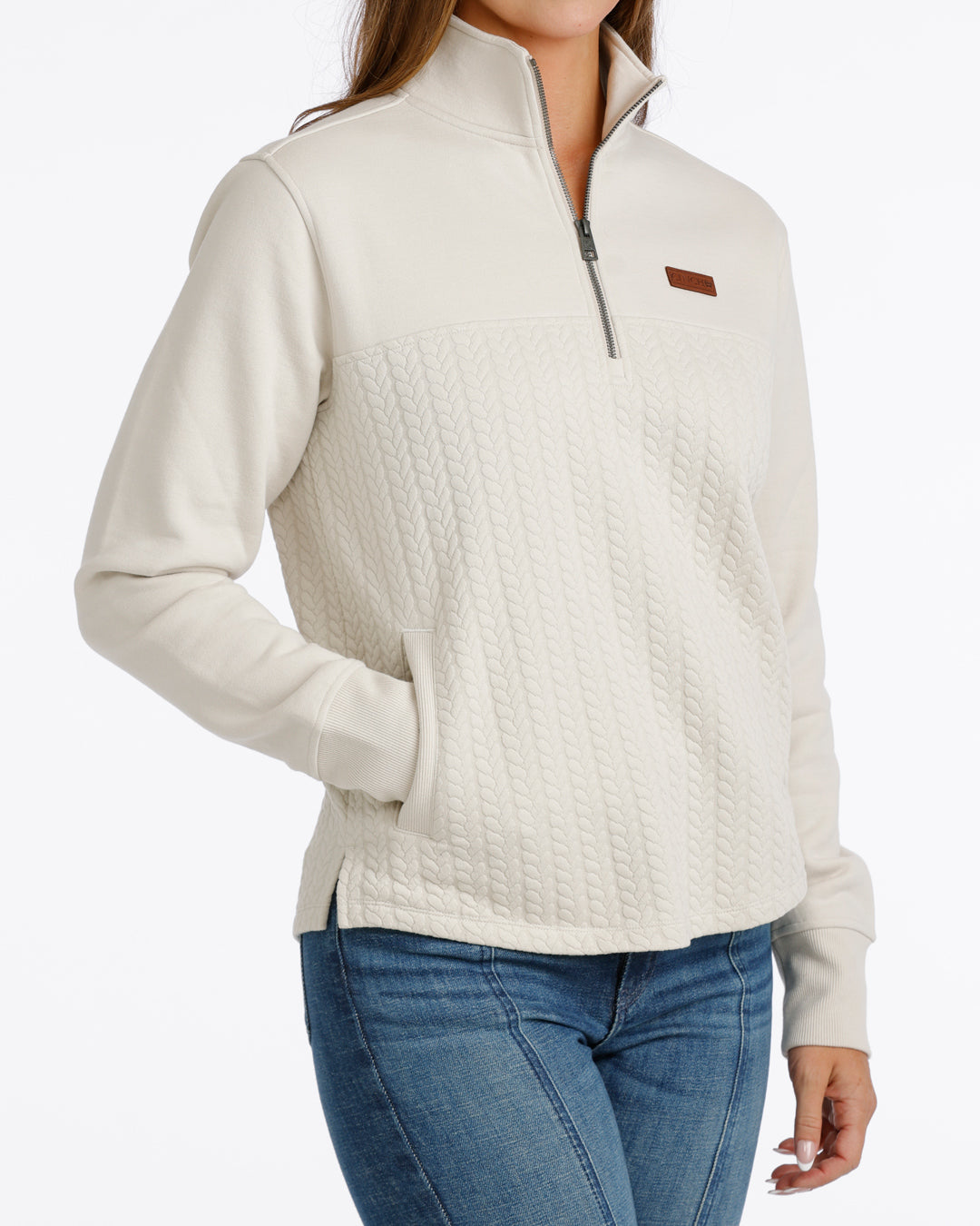 woman wearing a cream Cinch pullover sweater and blue jeans on a white background