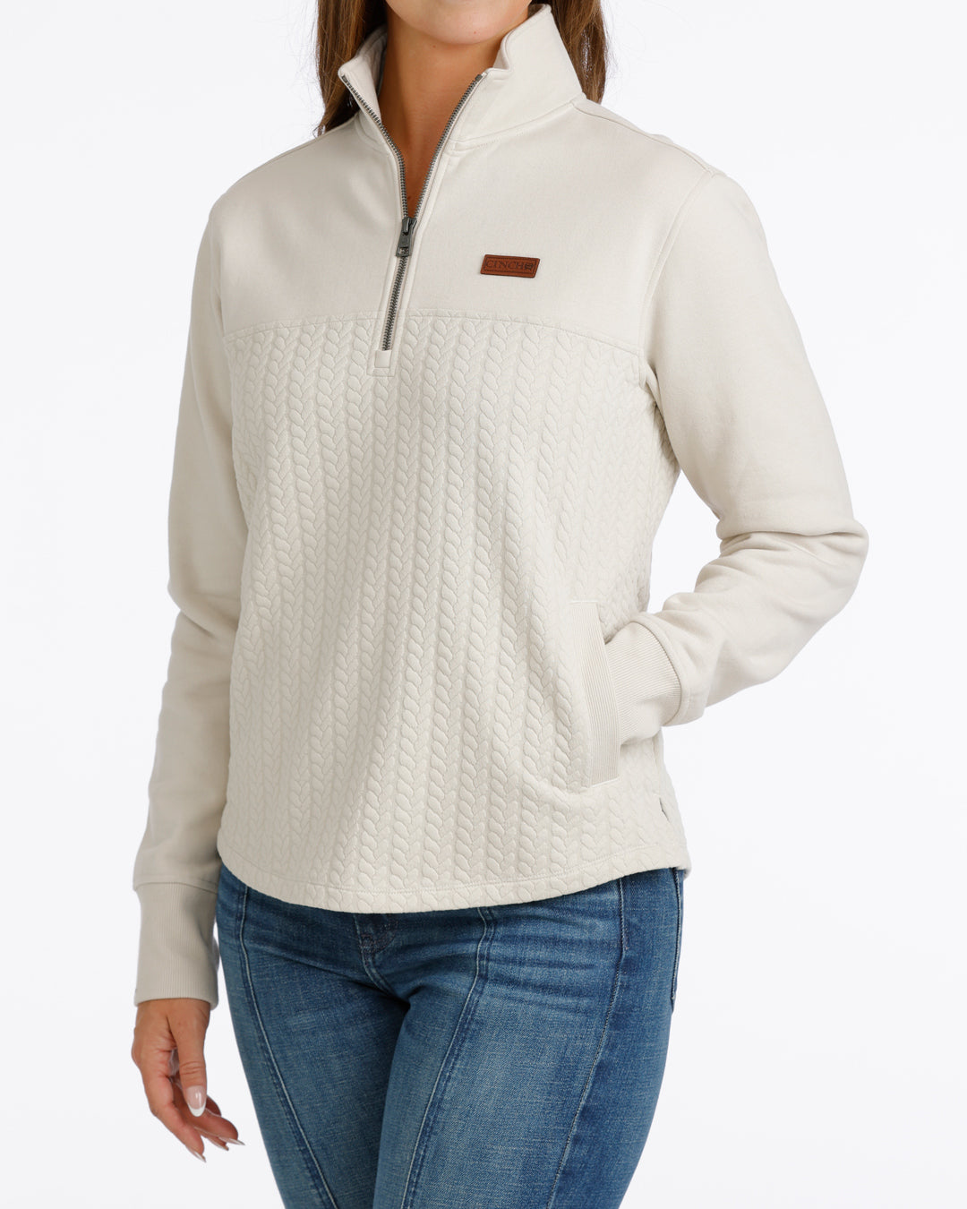 woman wearing a cream Cinch pullover sweater and blue jeans on a white background