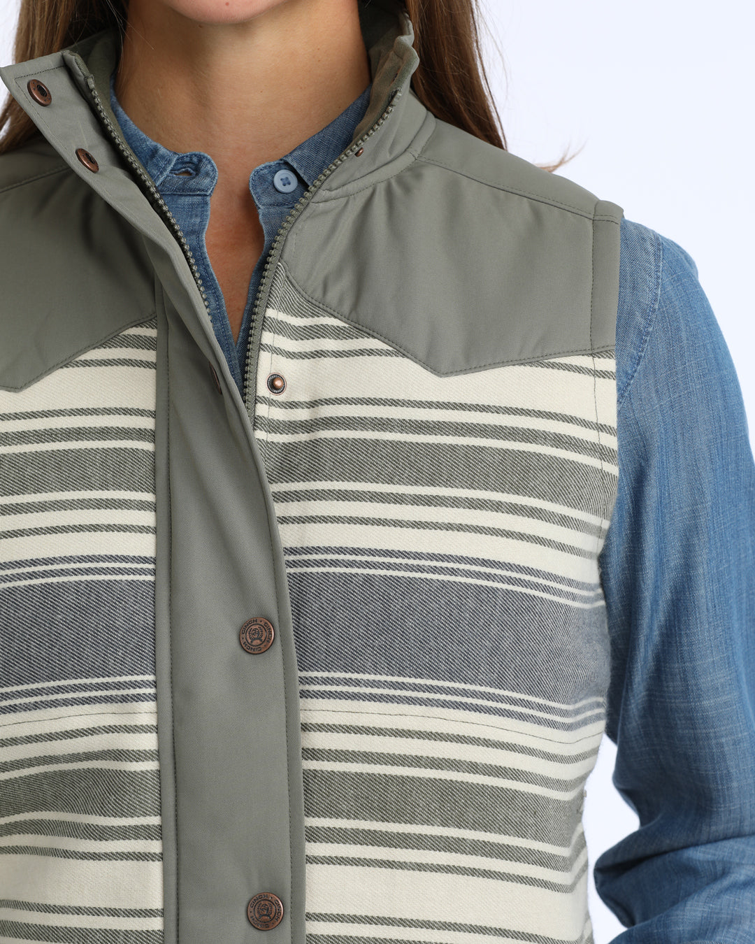Woman wearing a green and blue Cinch vest and a denim shirt on a white background