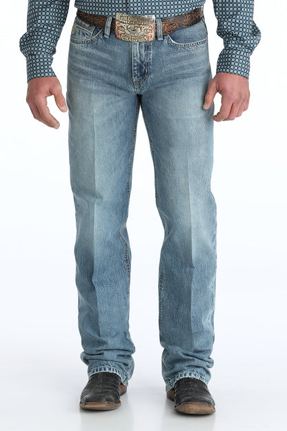 Person wearing relaxed light blue Cinch jeans with a patterned shirt and brown belt on a white background