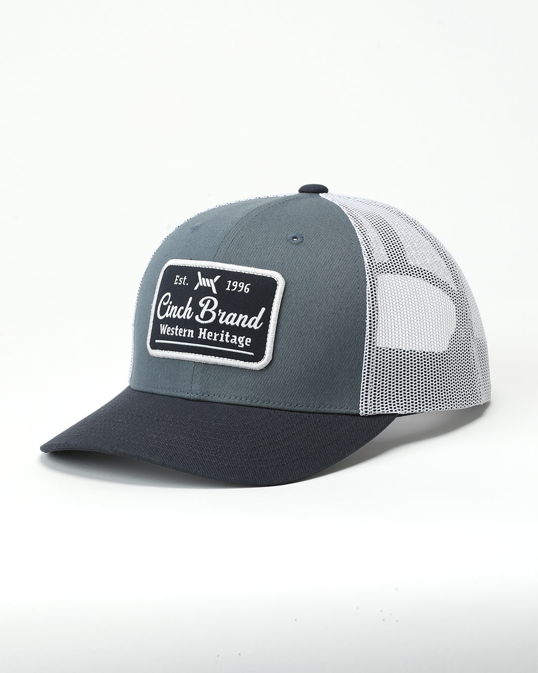A trucker-style baseball cap with a slate gray front panel, black brim, and white mesh back panels. The front panel features a rectangular patch that reads 'Cinch Brand Western Heritage' with 'Est.