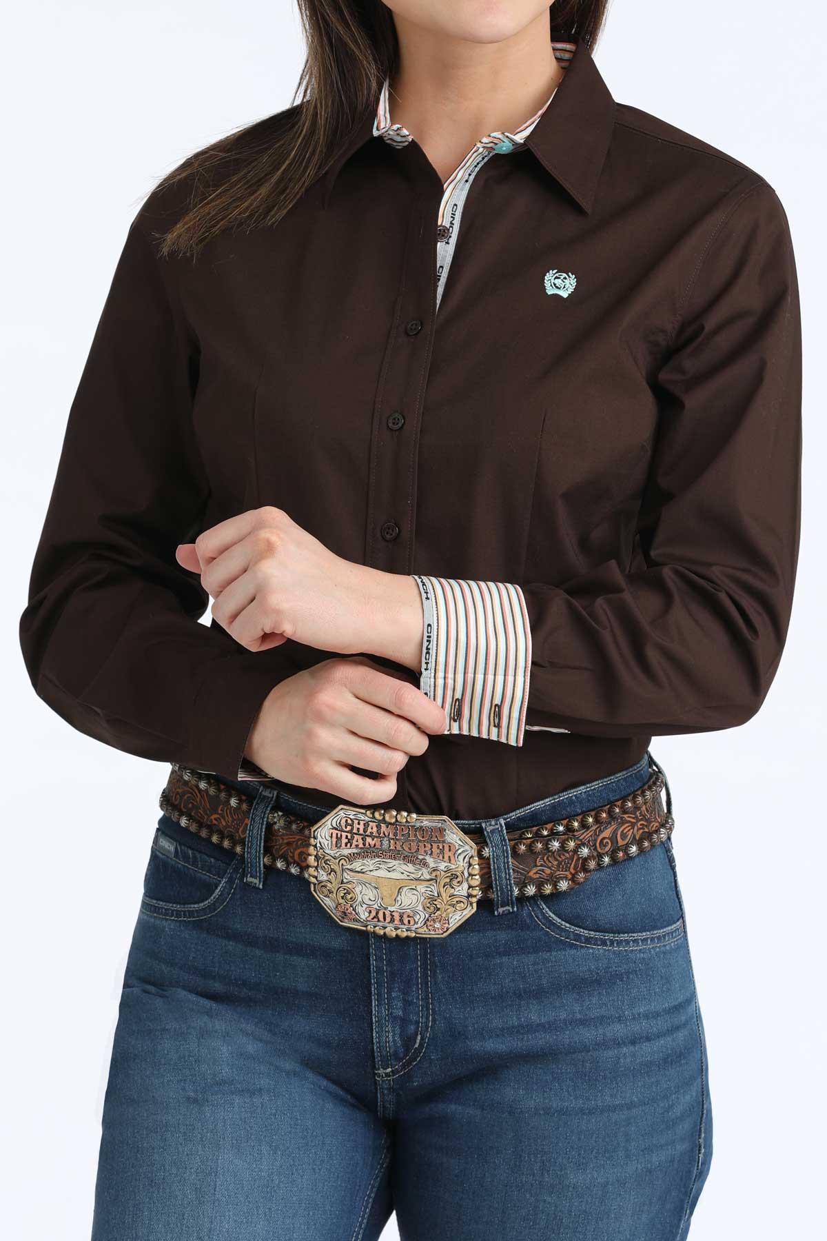 Woman wearing a brown 'Cinch' shirt and blue jeans with a decorative belt.