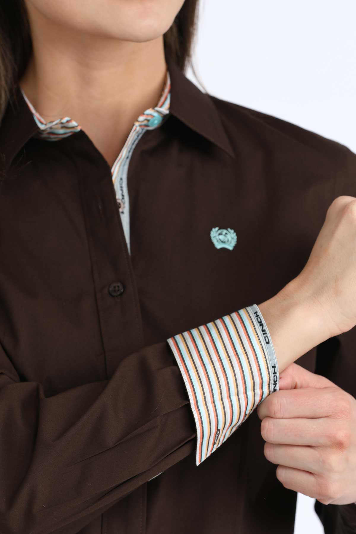 Woman wearing a brown 'Cinch' shirt with striped cuffs, adjusting the sleeve.