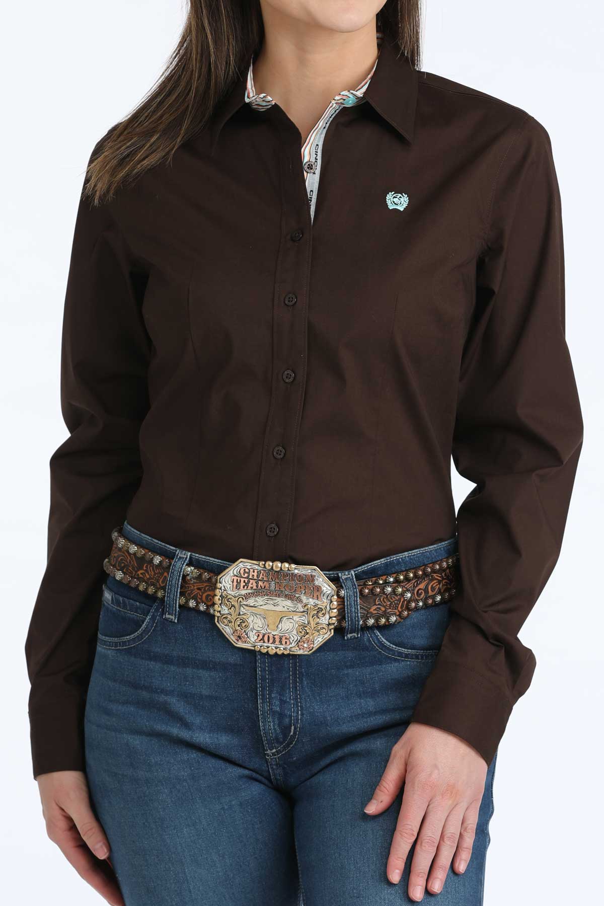 Woman wearing a brown button-up 'Cinch' shirt and blue jeans with a decorative belt on a white background