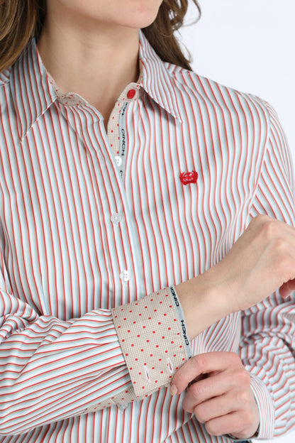 A close-up of a woman wearing a long-sleeve button-down Cinch shirt with thin red and white vertical stripes, featuring a small red embroidered heart on the chest and a patterned cuff.