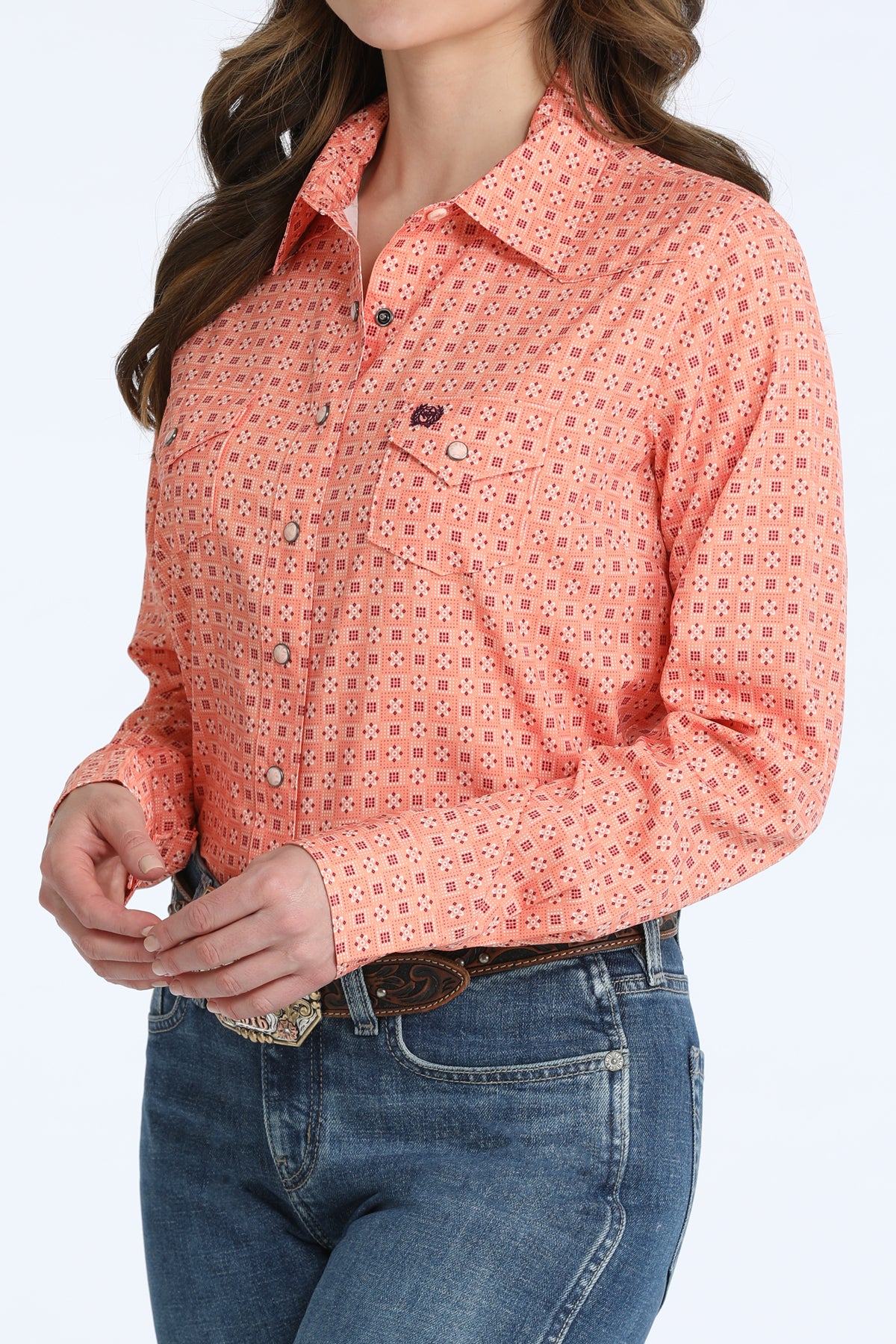 Woman wearing a coral Cinch patterned shirt and blue jeans with a belt.
