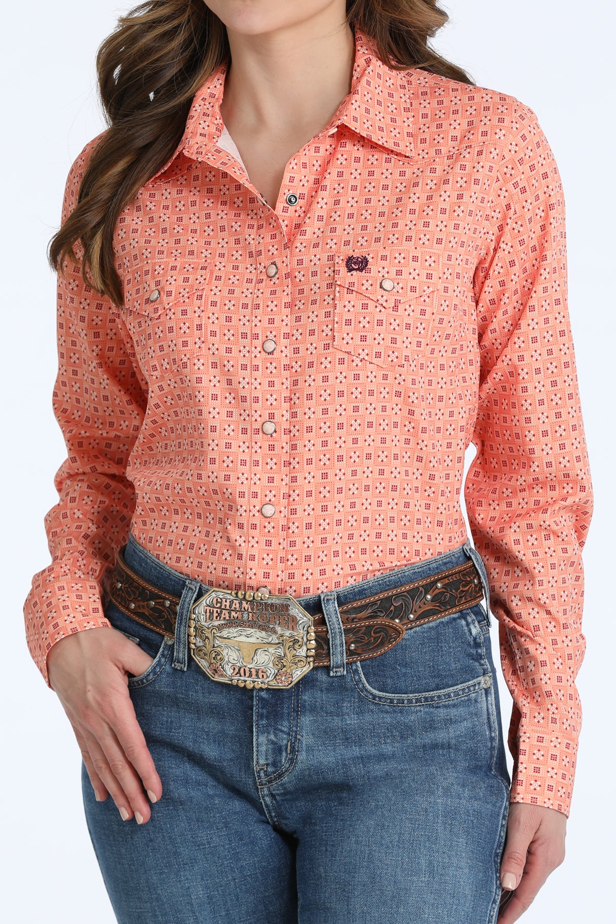 Woman wearing a coral Cinch patterned shirt and blue jeans with a belt.