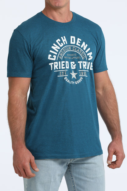 Person wearing a blue t-shirt with 'Cinch Denim Tried & True' text on a white background