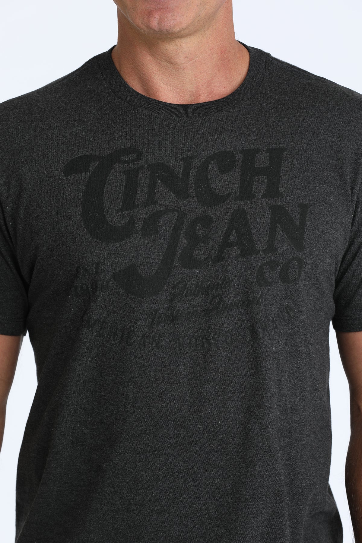 A close-up of a man wearing a dark heather gray t-shirt with a faded black graphic print that reads 'Cinch Jean Co'.