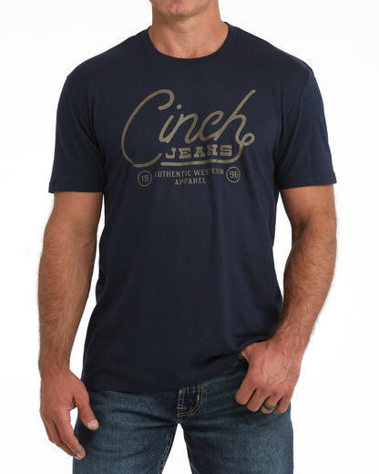 man wearing a navy Cinch tshirt with writing on the front, and blue jeans on a white background