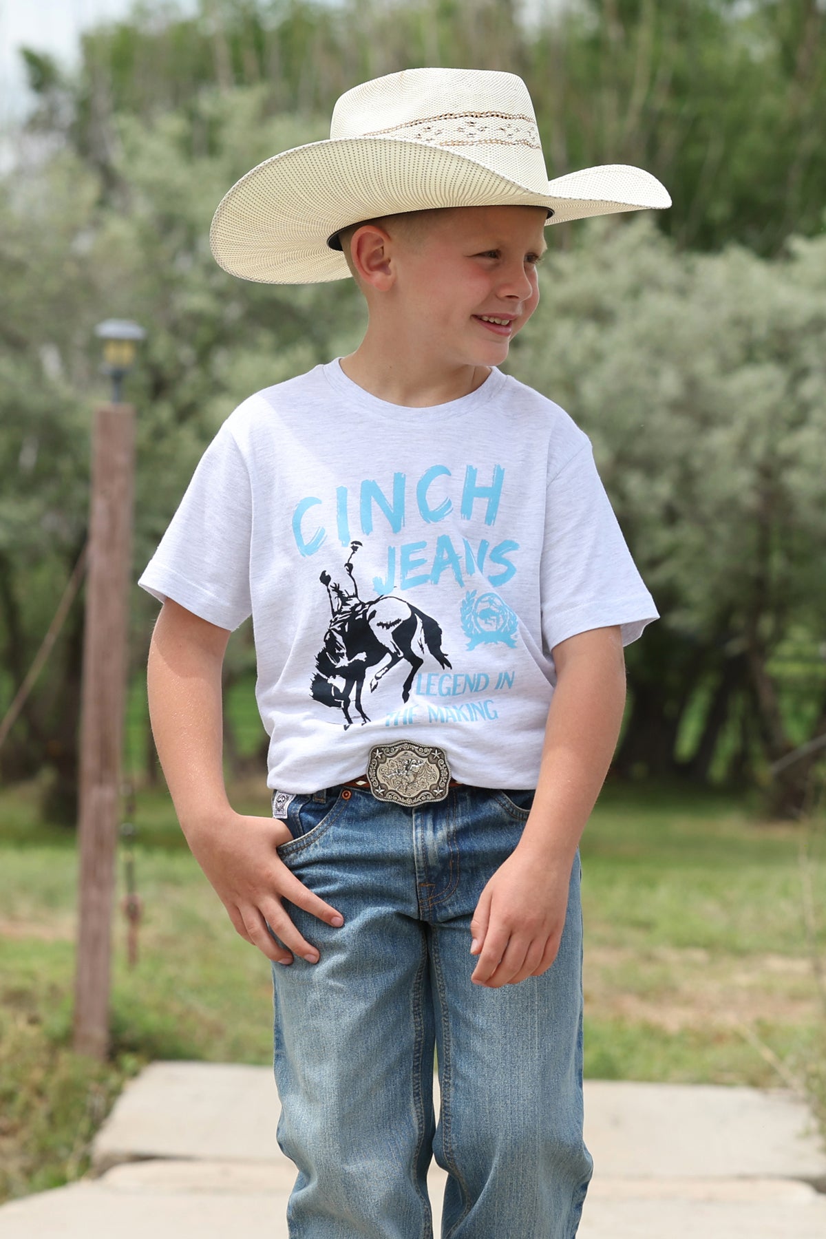 boy wearing grey Cinch shirt and blue jeans and a cowboy hat