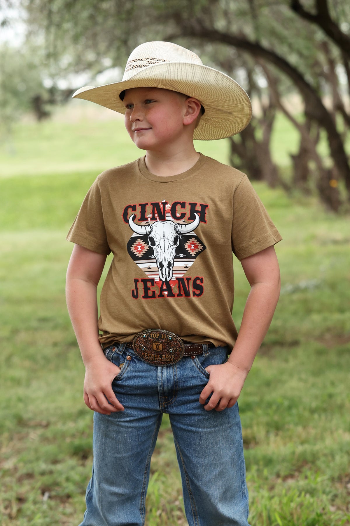 boy wearing a brown Cinch shirt with blue jeans and a cowboy hat