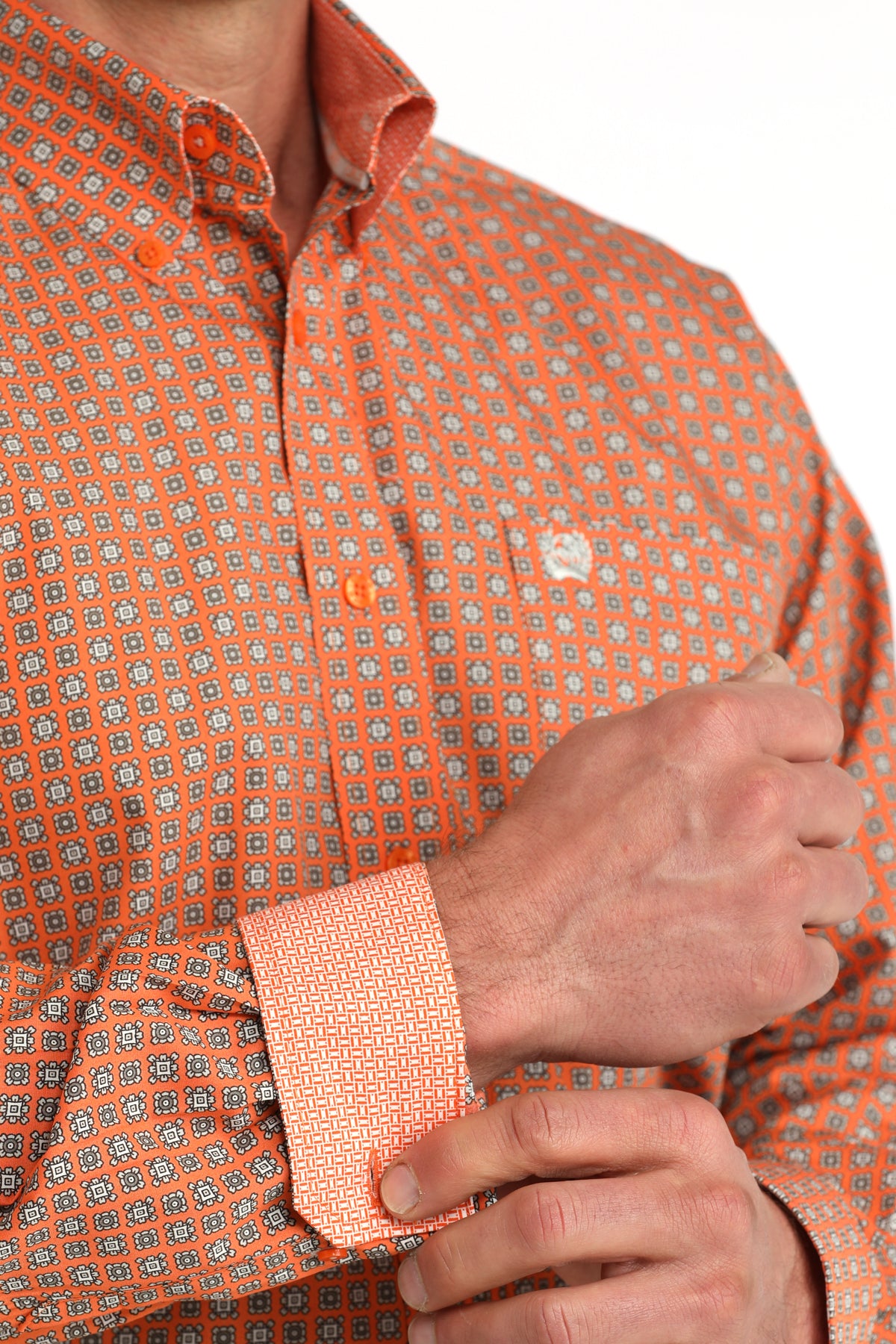 Close-up of an orange patterned 'Cinch' shirt with a person adjusting the sleeve.