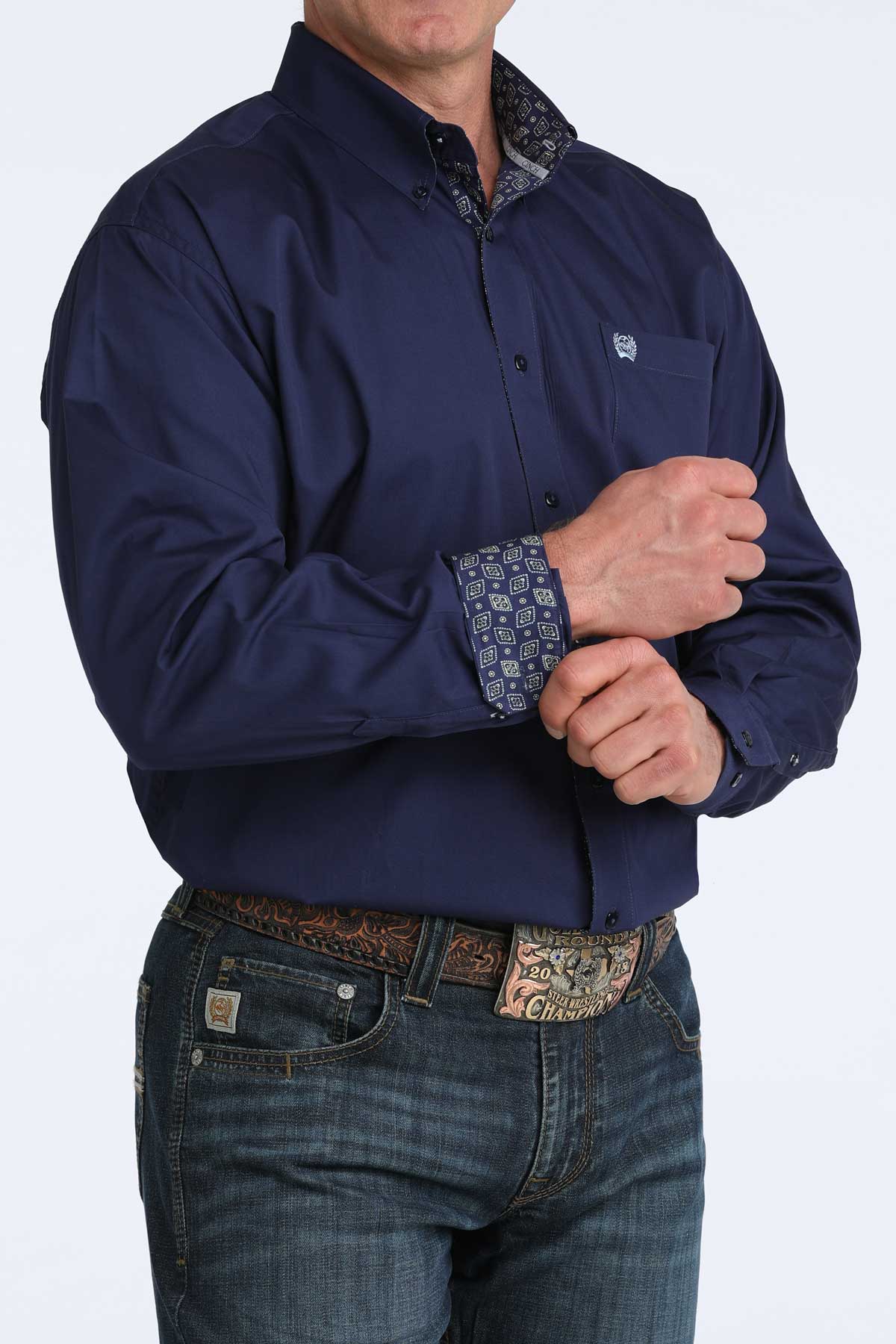 Man wearing a navy blue cinch shirt with patterned cuffs and jeans on a white background