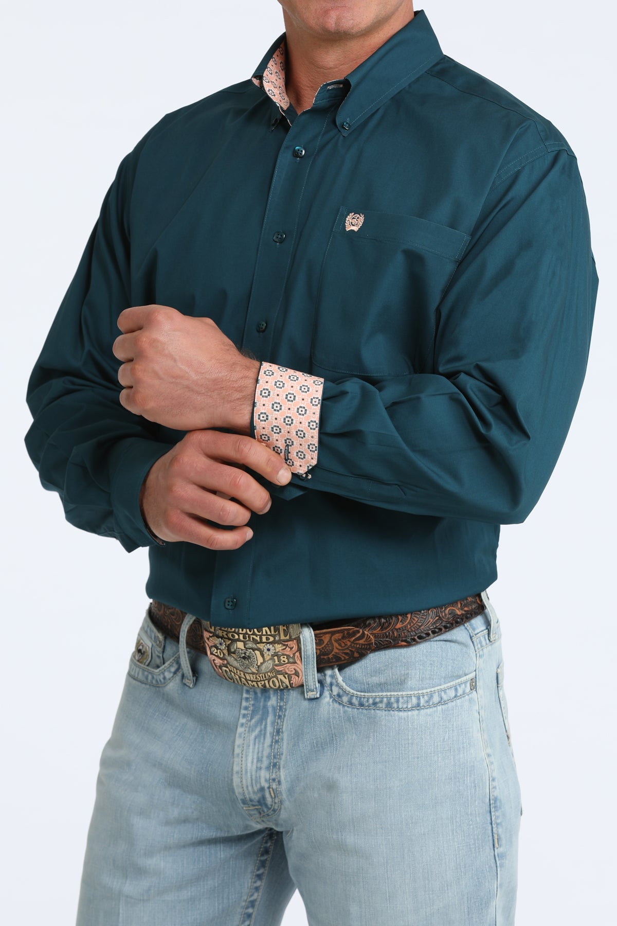 Man wearing a teal Cinch shirt with rolled-up sleeves and light blue jeans on a white background