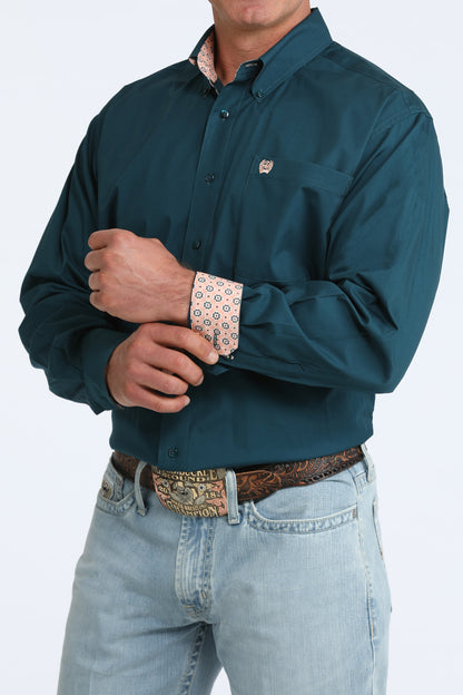 Man wearing a teal Cinch shirt with rolled-up sleeves and light blue jeans on a white background