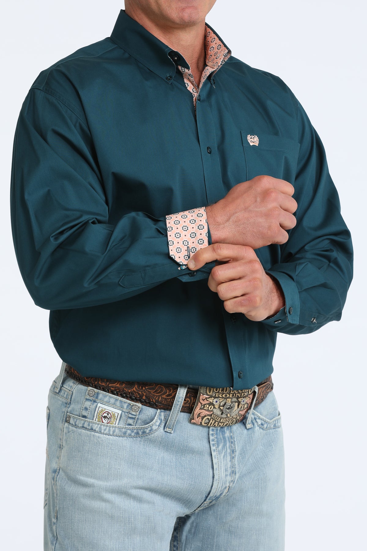 Man wearing a teal Cinch shirt with rolled-up sleeves and light blue jeans on a white background