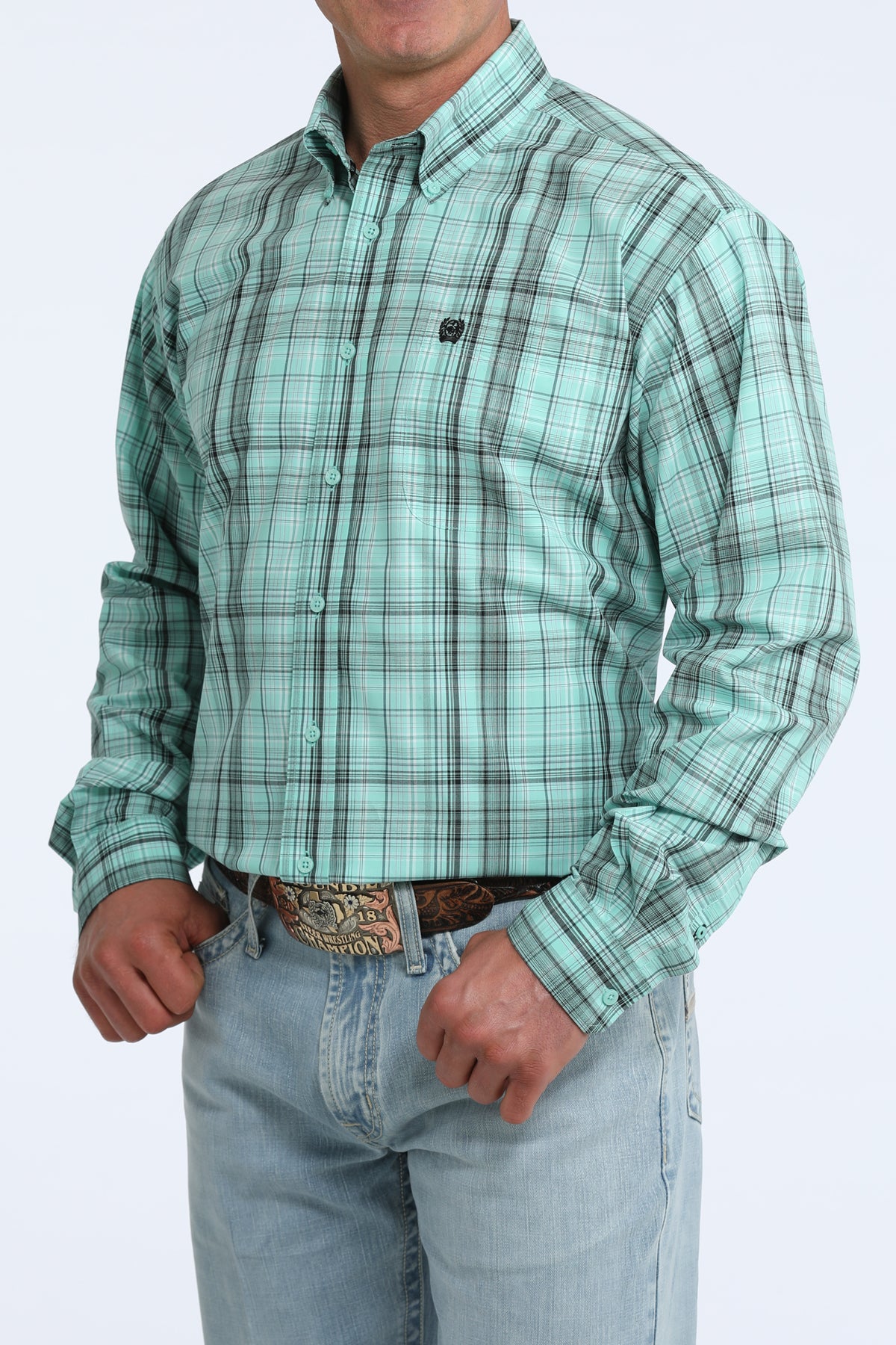 Man wearing a green plaid Cinch shirt and light blue jeans on a white background