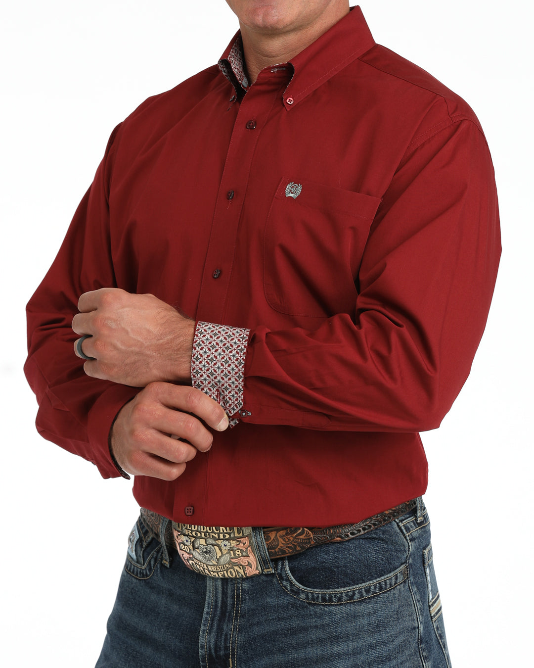 A man wearing a red long-sleeve button-down Cinch shirt with a patterned cuff, paired with blue jeans and a western belt buckle, shown against a plain white background.