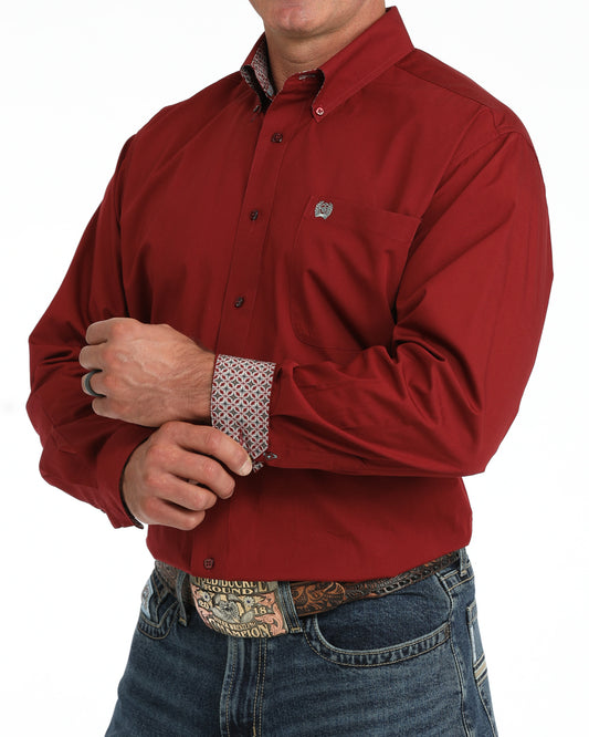 A man wearing a red long-sleeve button-down Cinch shirt with a patterned cuff, paired with blue jeans and a western belt buckle, shown against a plain white background.