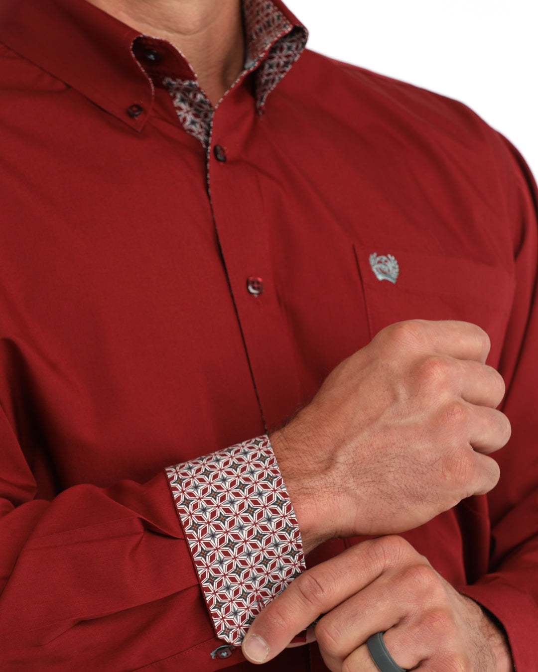 A close-up of a man wearing a red button-down Cinch shirt with a patterned inner collar and matching patterned cuff, adjusting the cuff with one hand.