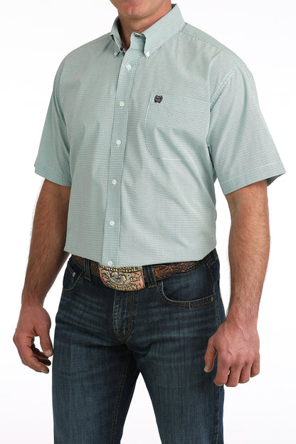 Man wearing a light blue short-sleeve button-up 'Cinch' shirt and dark jeans on a white background