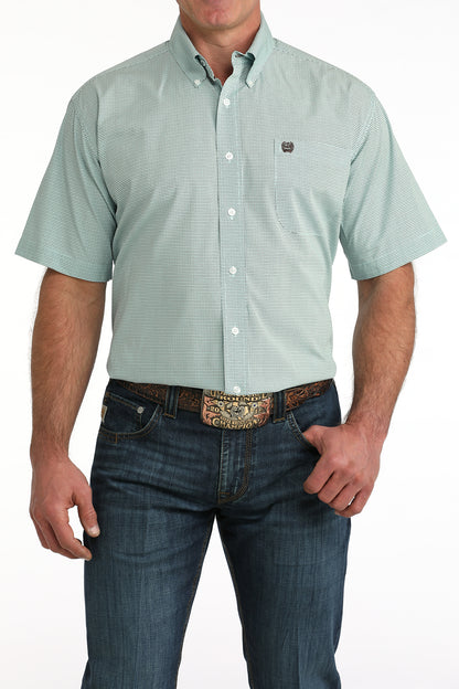Man wearing a light blue short-sleeve button-up 'Cinch' shirt and dark jeans on a white background