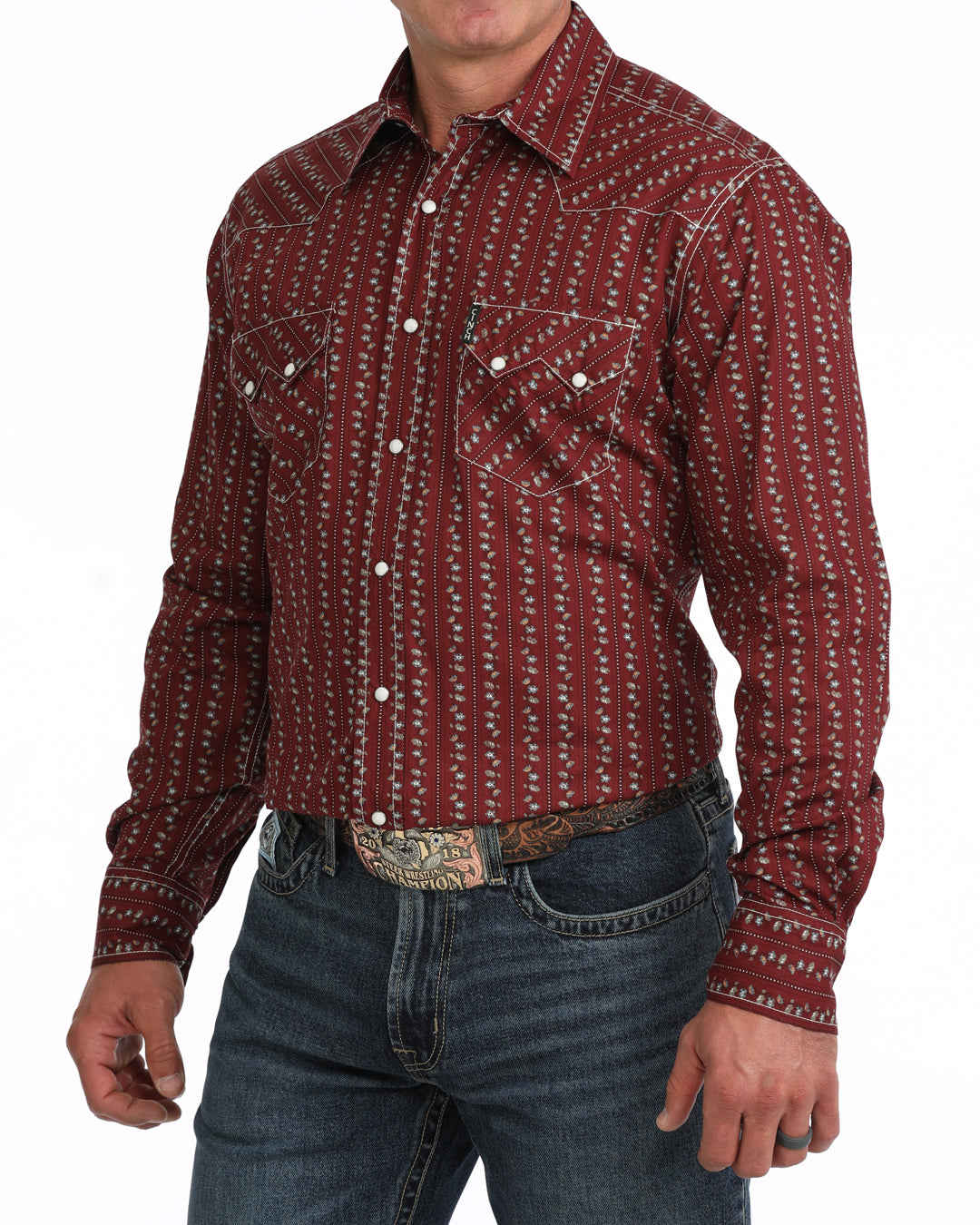 A man wearing a long-sleeve western-style button-up Cinch shirt with a red and white vertical patterned design, paired with blue jeans and a western belt.