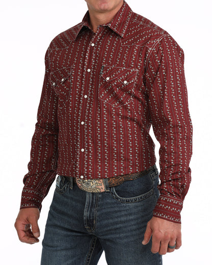 A man wearing a long-sleeve western-style button-up Cinch shirt with a red and white vertical patterned design, paired with blue jeans and a western belt.