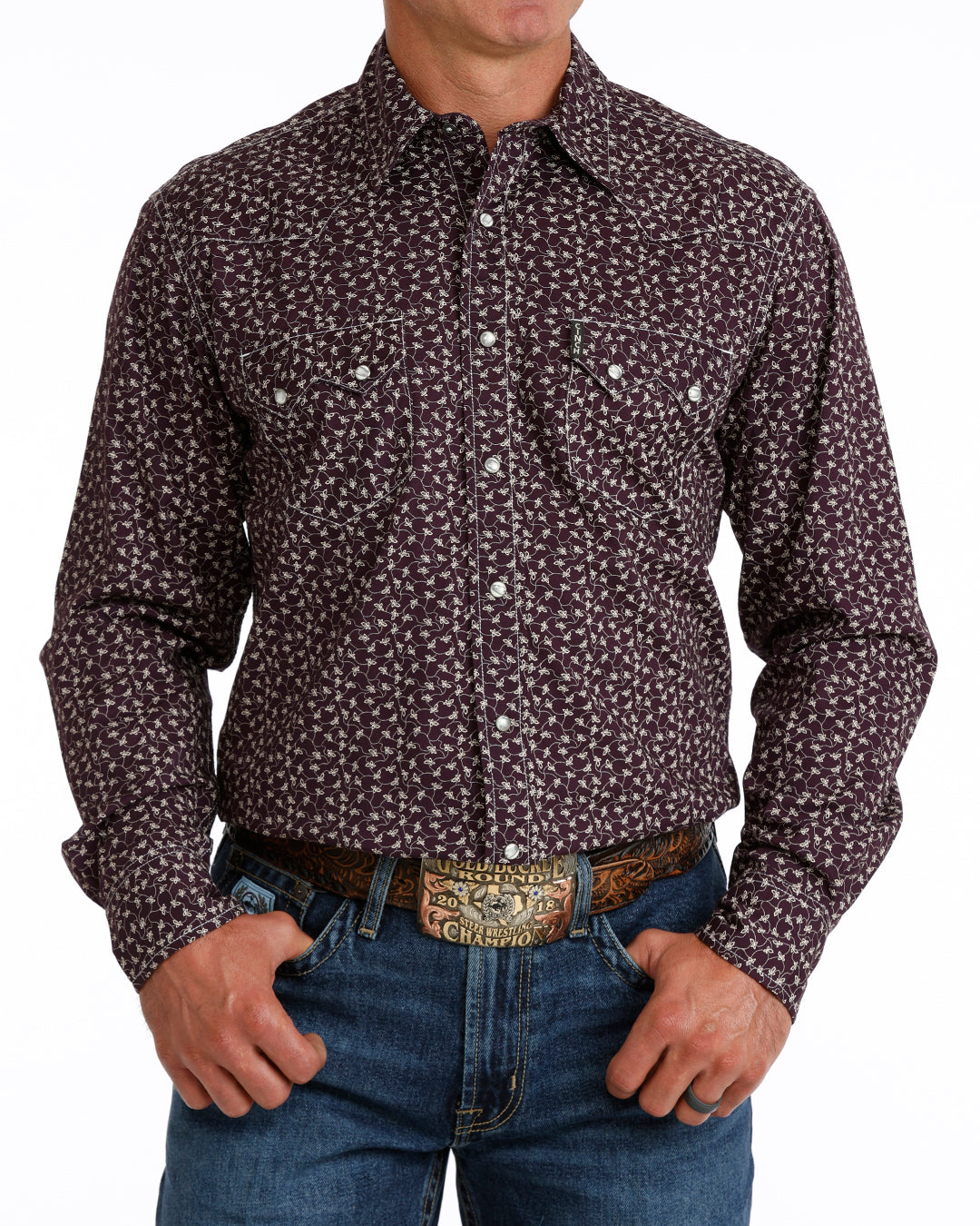 Man wearing a purple floral Cinch shirt and blue jeans on a white background