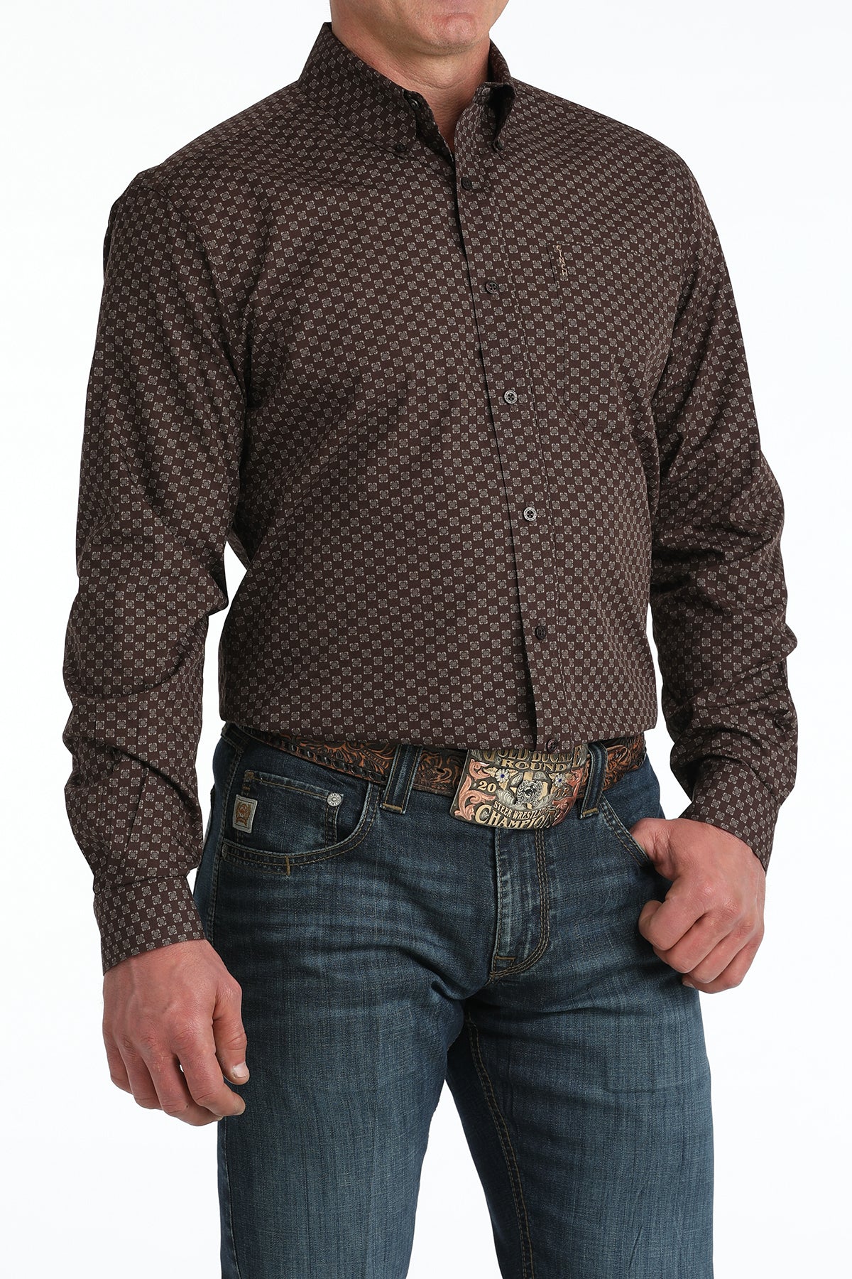 Man wearing a patterned brown 'Cinch' shirt and blue jeans with a belt buckle.