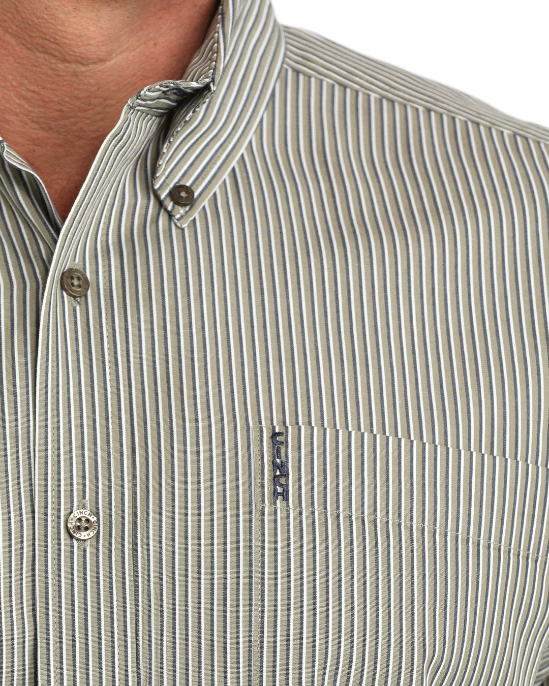 Close-up of a man wearing a button-down Cinch shirt with thin vertical gray and white stripes, featuring a chest pocket with a small blue and white logo tag.