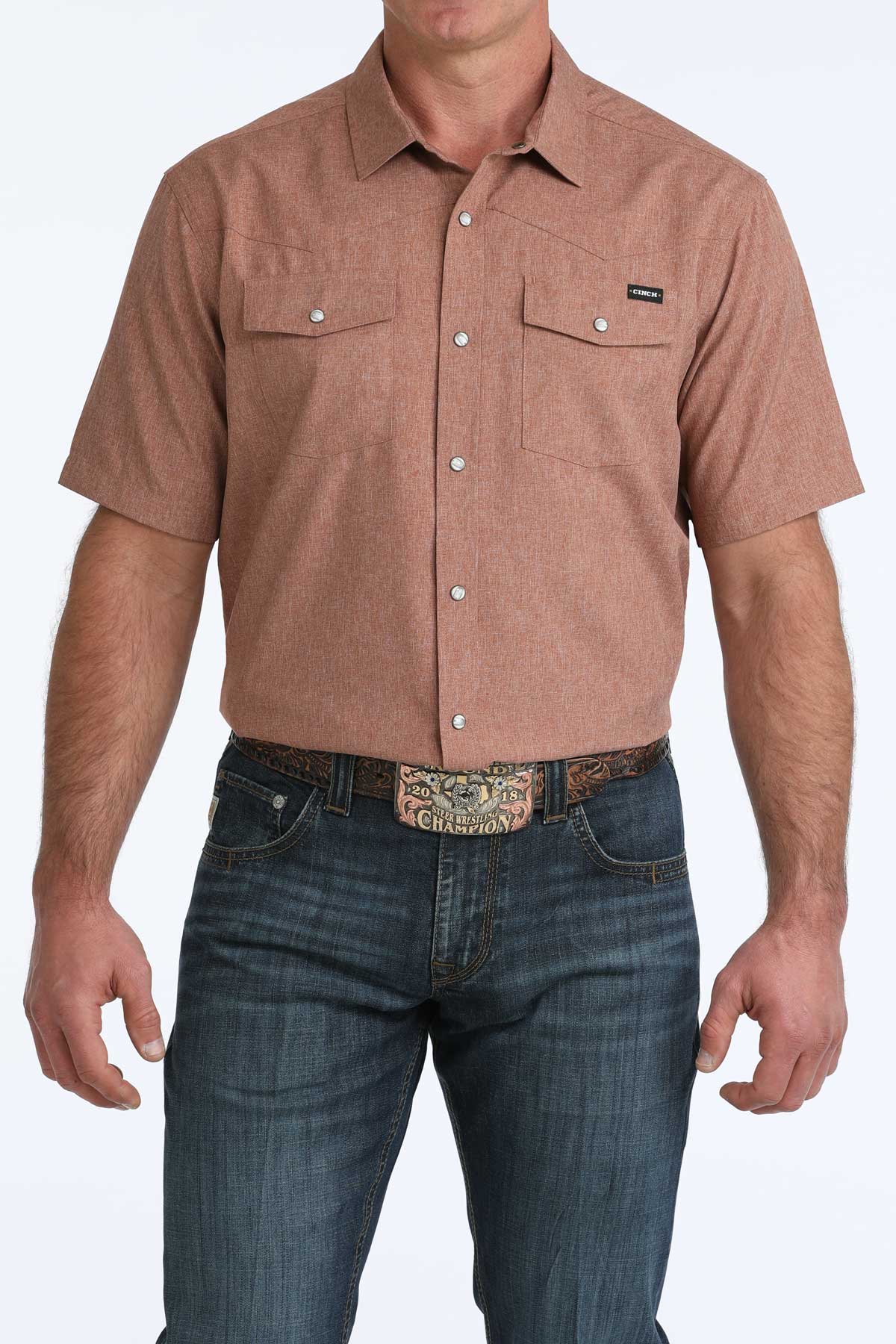Man wearing a brown short-sleeve 'Cinch' shirt and blue jeans on a white background