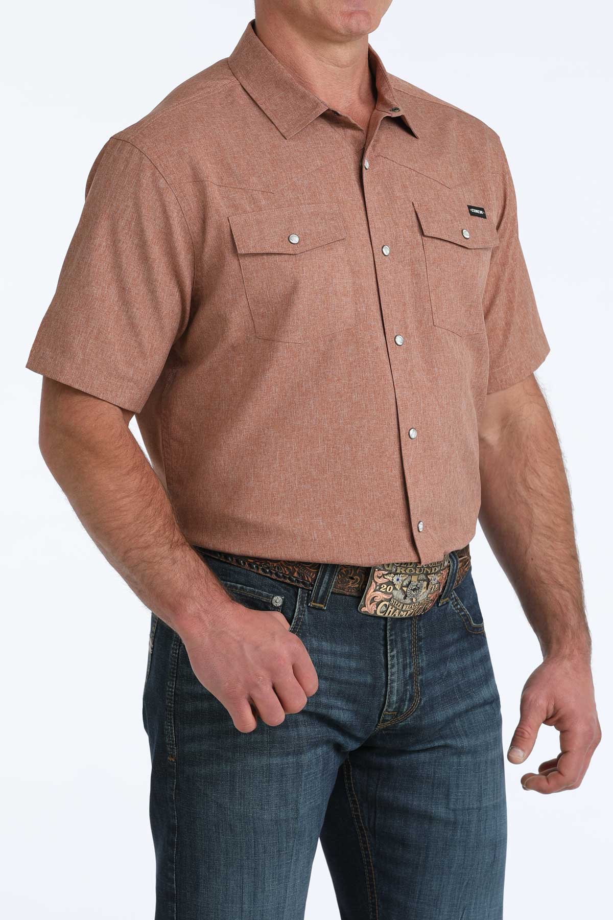 Man wearing a brown short-sleeve 'Cinch' shirt and blue jeans on a white background